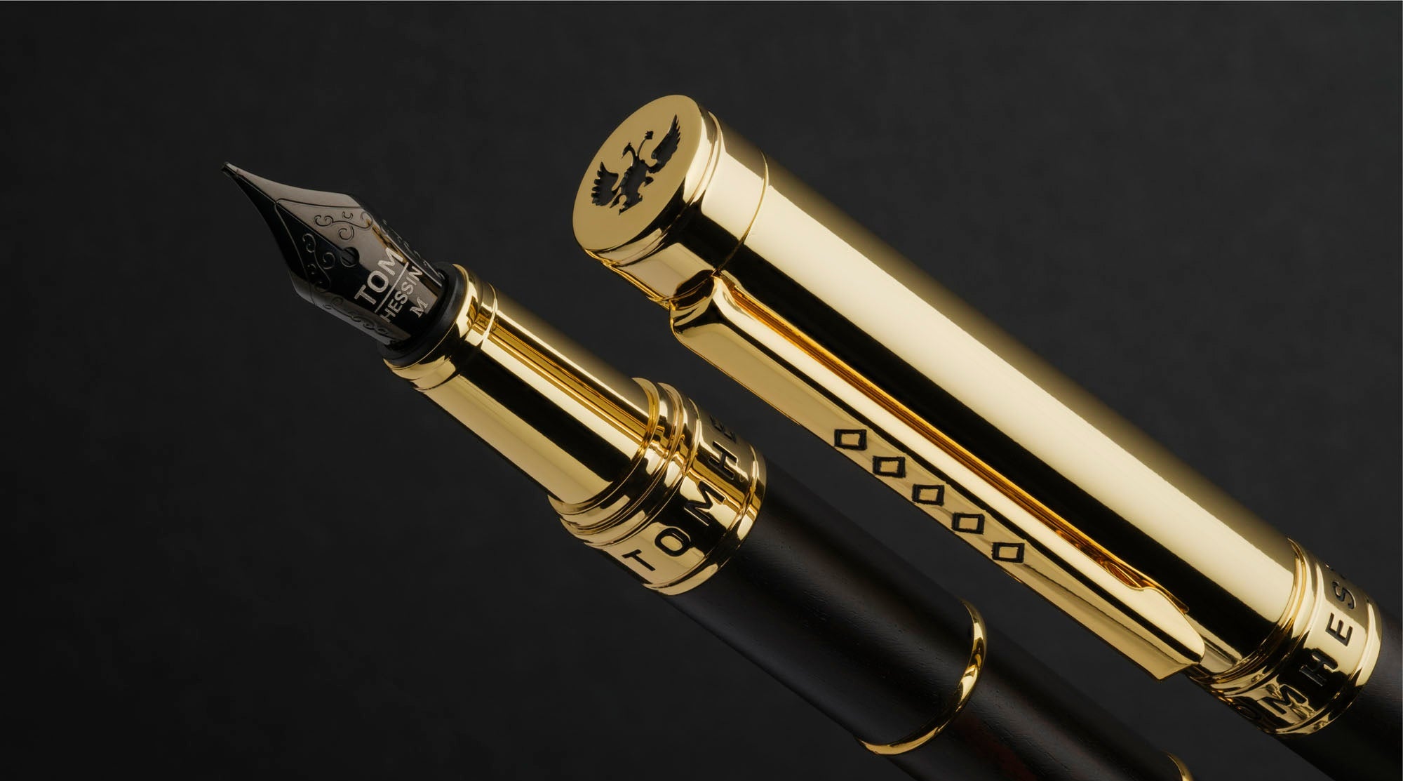 A luxury fountain pen with a glossy black barrel and polished gold-tone metal accents, shown with its cap removed against a dark background. The nib is engraved with 'EST.