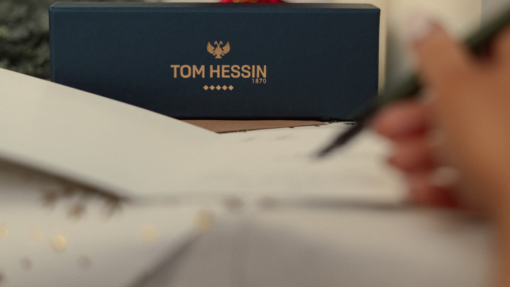 TOM Hessin box with a blurred background of candles and a decorative item.