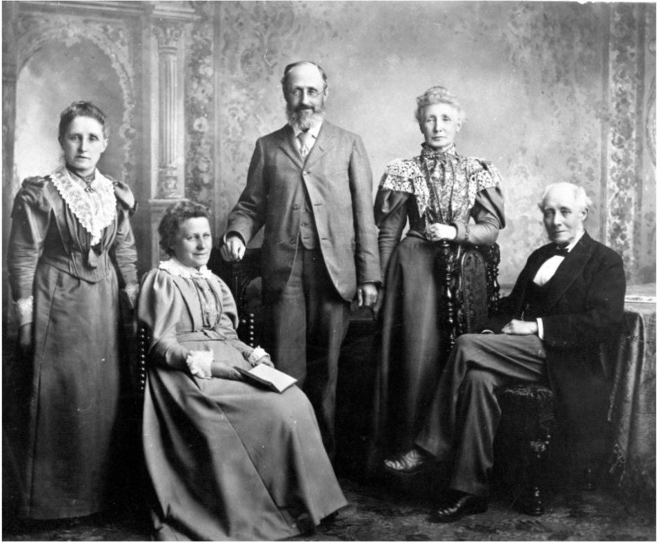 Victorian studio photograph of five people: two women and a man standing, a woman and an older man seated