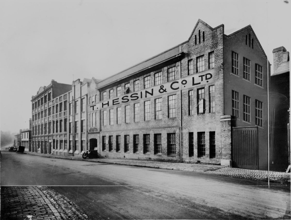 Black and white photograph of a four-storey brick factory on a cobbled street, with T. Hessin and Co. Ltd painted across the front